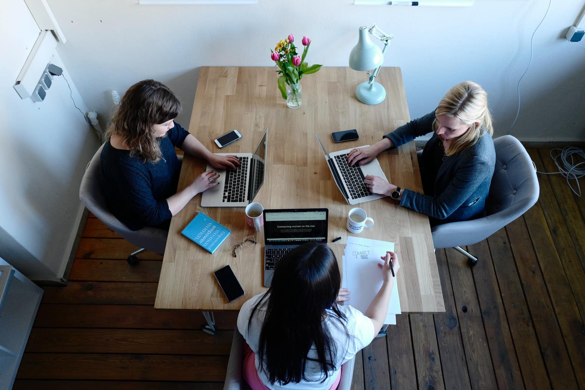 A imagem mostra três mulheres atuando como headhunters, trabalhando com seus computadores sobre uma mesa