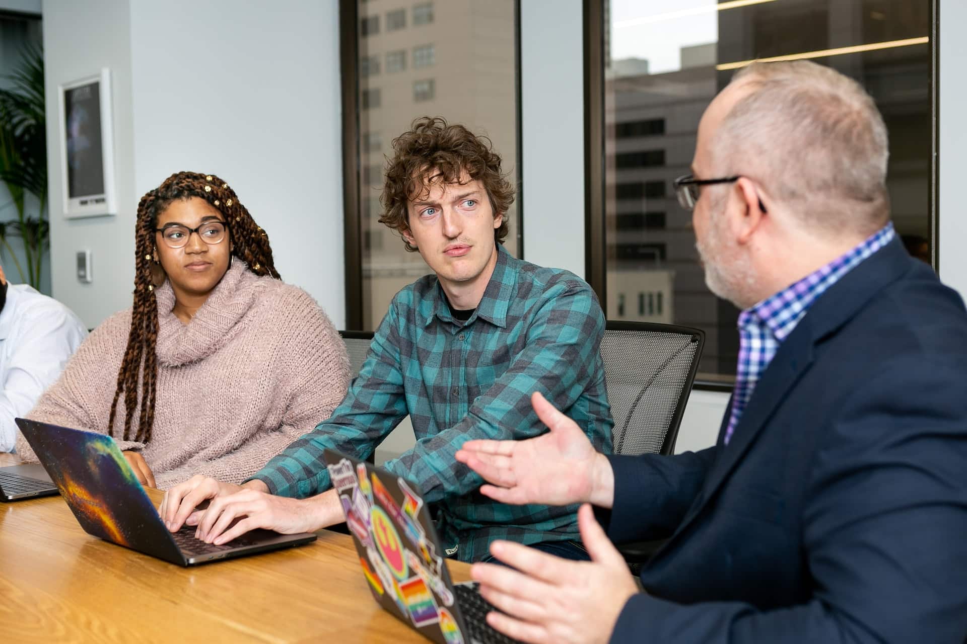 A imagem mostra um homem branco, no papel de programador sênior, orientando demais profissionais da equipe, representados por uma mulher negra e um homem branco, ambos jovens